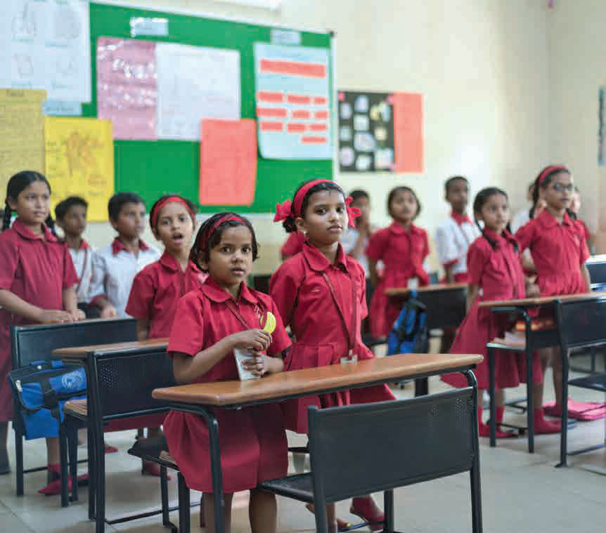Schoolgirls in red uniforms attending a classroom supported by Bajaj Finserv's CSR programmes.