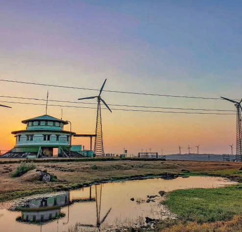 Wind turbines at dusk beside a green watchtower at Bajaj Finserv's Maharashtra wind site.