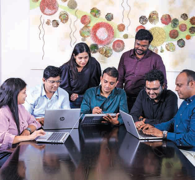 A team of Bajaj Finserv colleagues working together on laptops around a table.